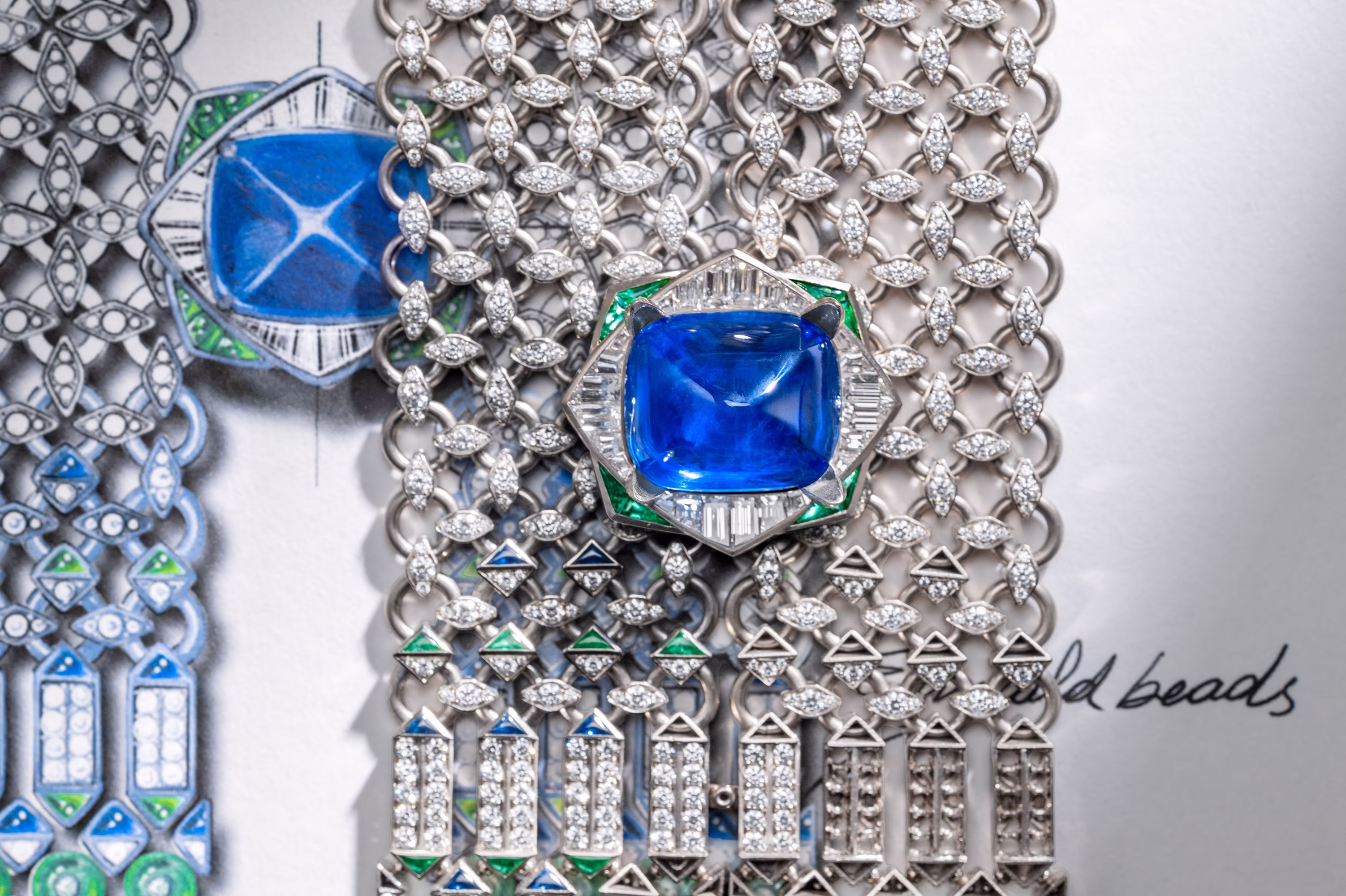 Close-up of diamond necklace with large blue sapphire centerpiece, placed over a detailed jewelry design drawing.
